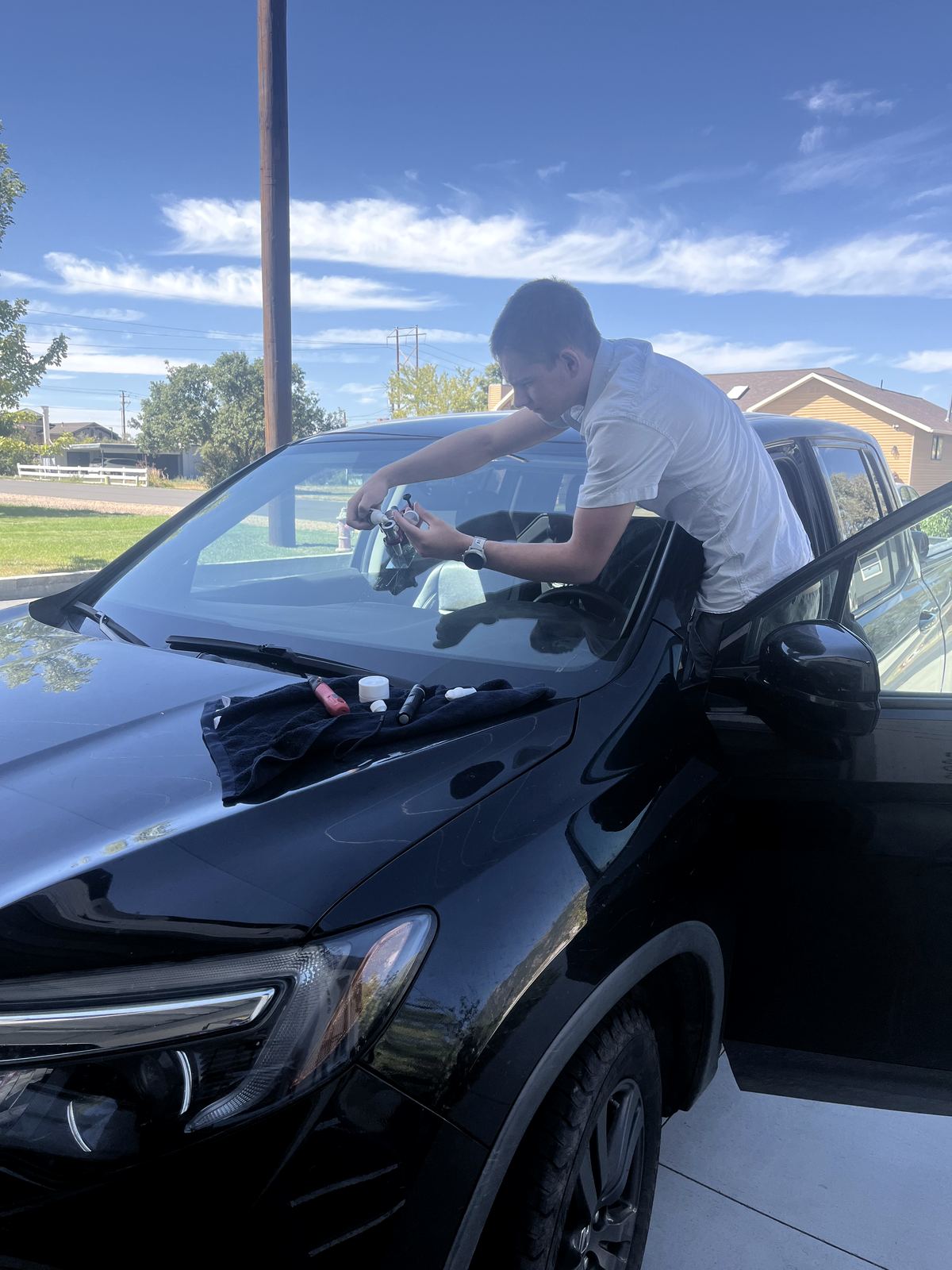 James leaning through the door of a black SUV in a driveway, working a chip on the windshield, tools laid out on the hood.